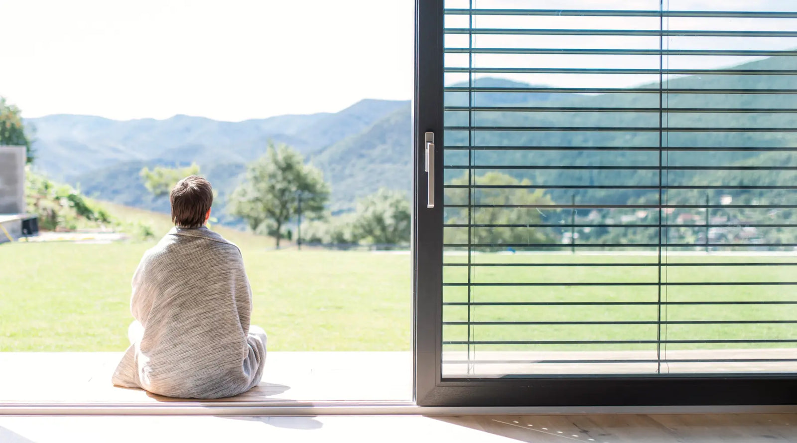 Person wrapped in a blanket, sitting on porch outside of open door, enjoying clean air