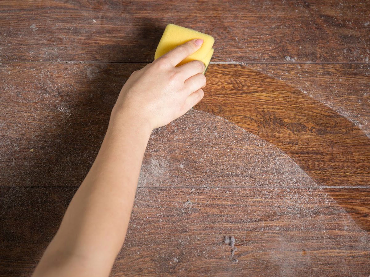 A hand wiping a wooden surface free of dust with a yellow sponge