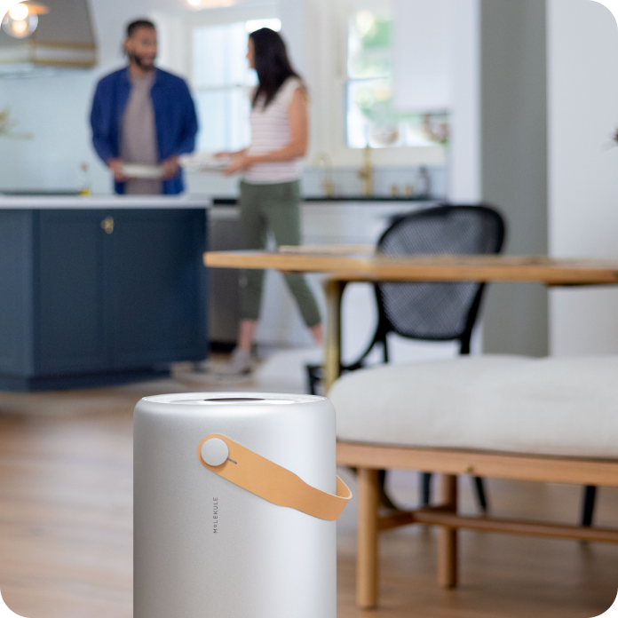 Molekule Air Pro purifier in focus while two friends preparing dinner together in the background