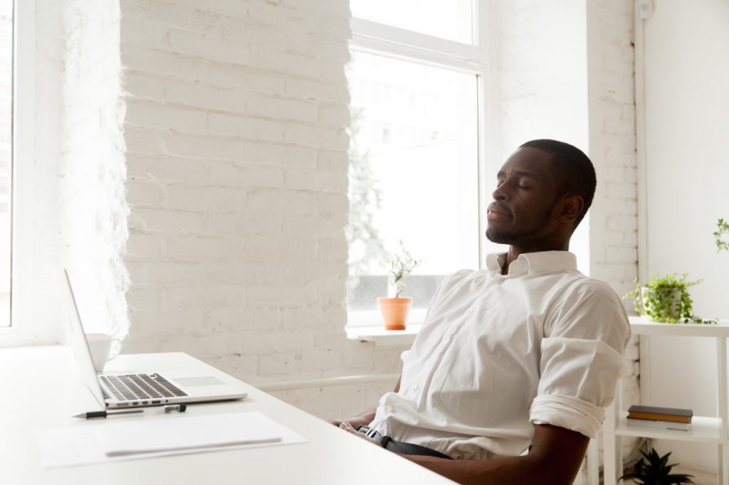 Black man sitting at a desk breathing relaxed with a laptop