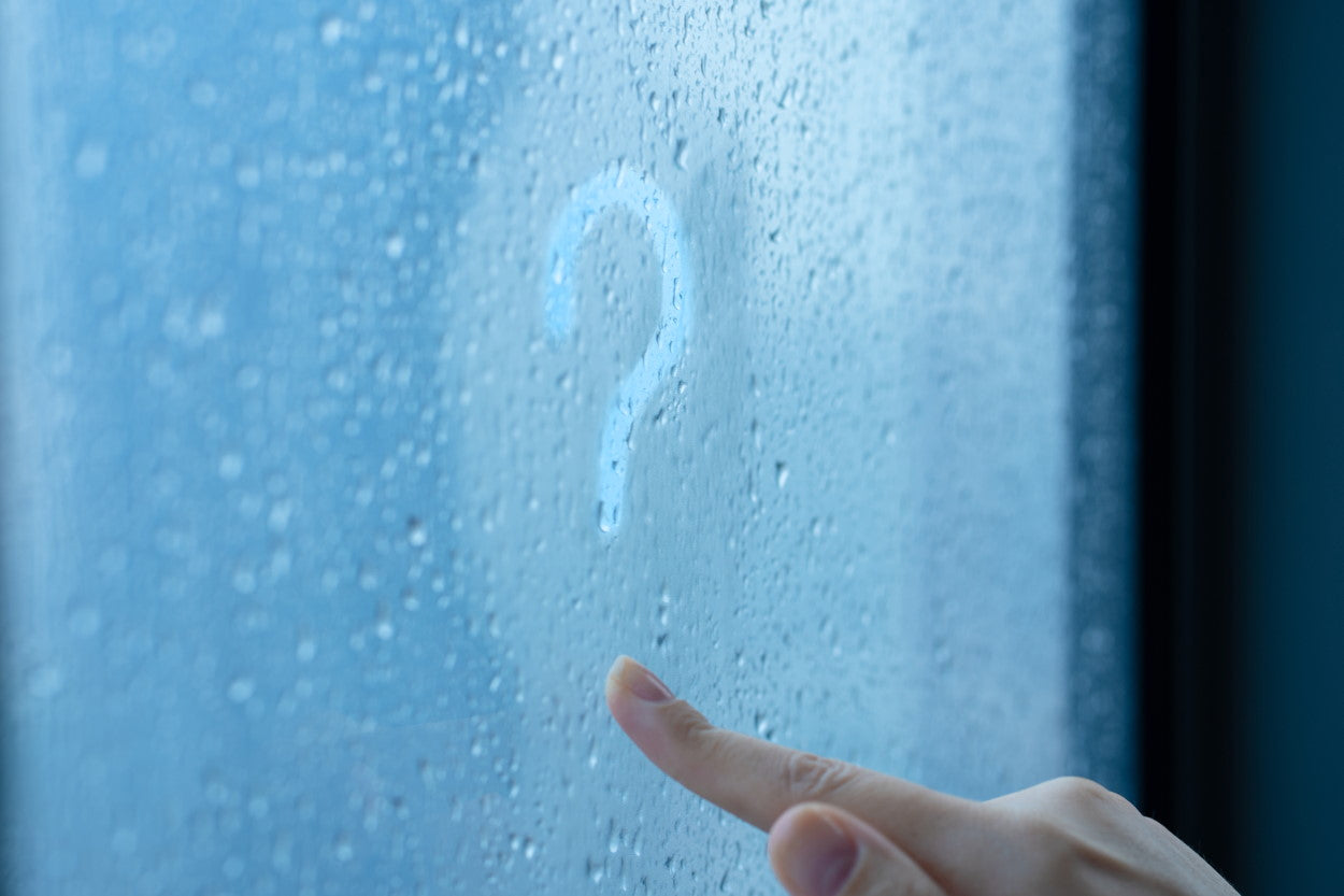 Question mark drawn in condensation on a window by a woman's hand