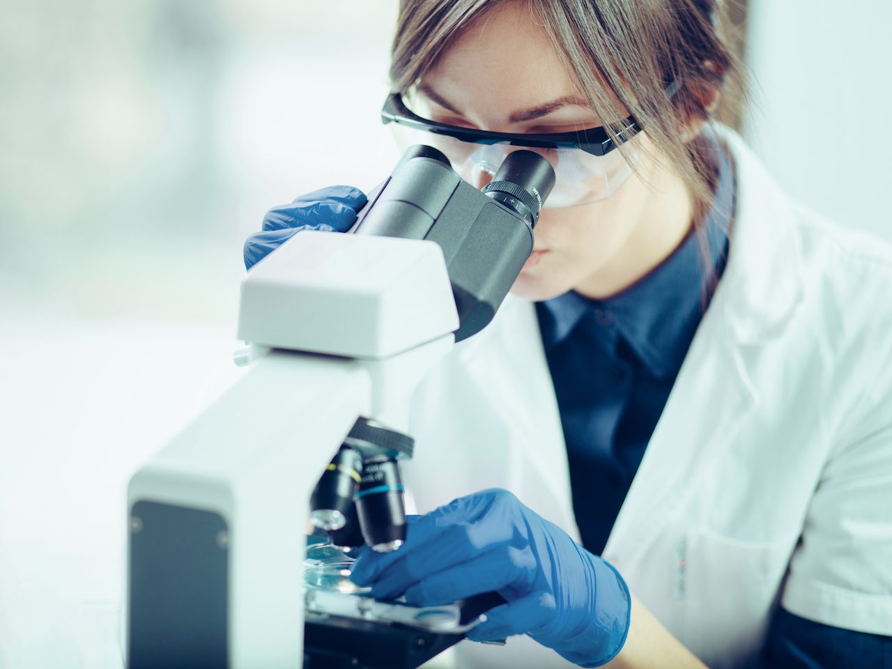 A woman in a lab coat looks through a microscope