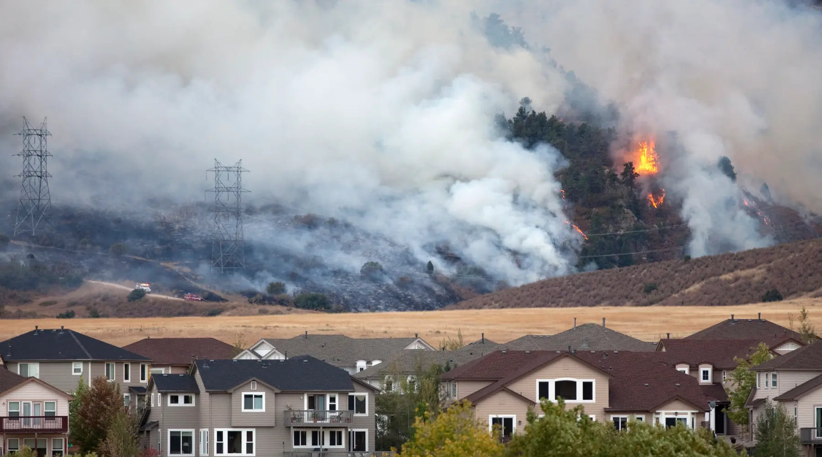 Wildfires in the distance beyond a residential neighborhood release large amounts of smoke into the air.