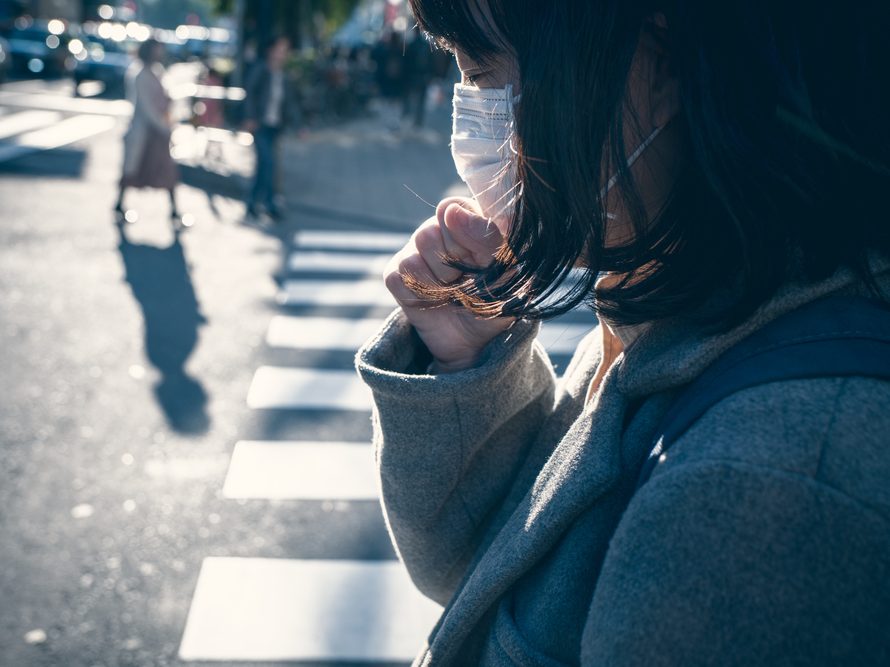 Woman with protective facemask coughing into her hand