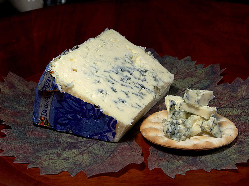 Chunks of blue cheese on cracker next to blue cheese wedge