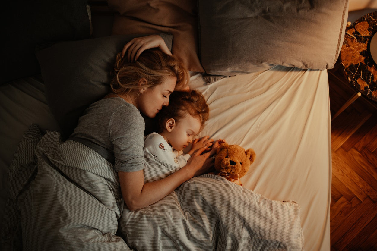 Woman cuddling with toddler and teddy bear in bed