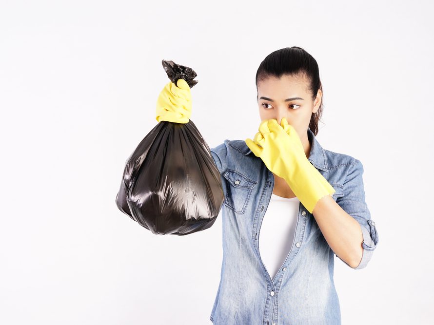 Woman plugging her nose as she takes out smelly trash bag