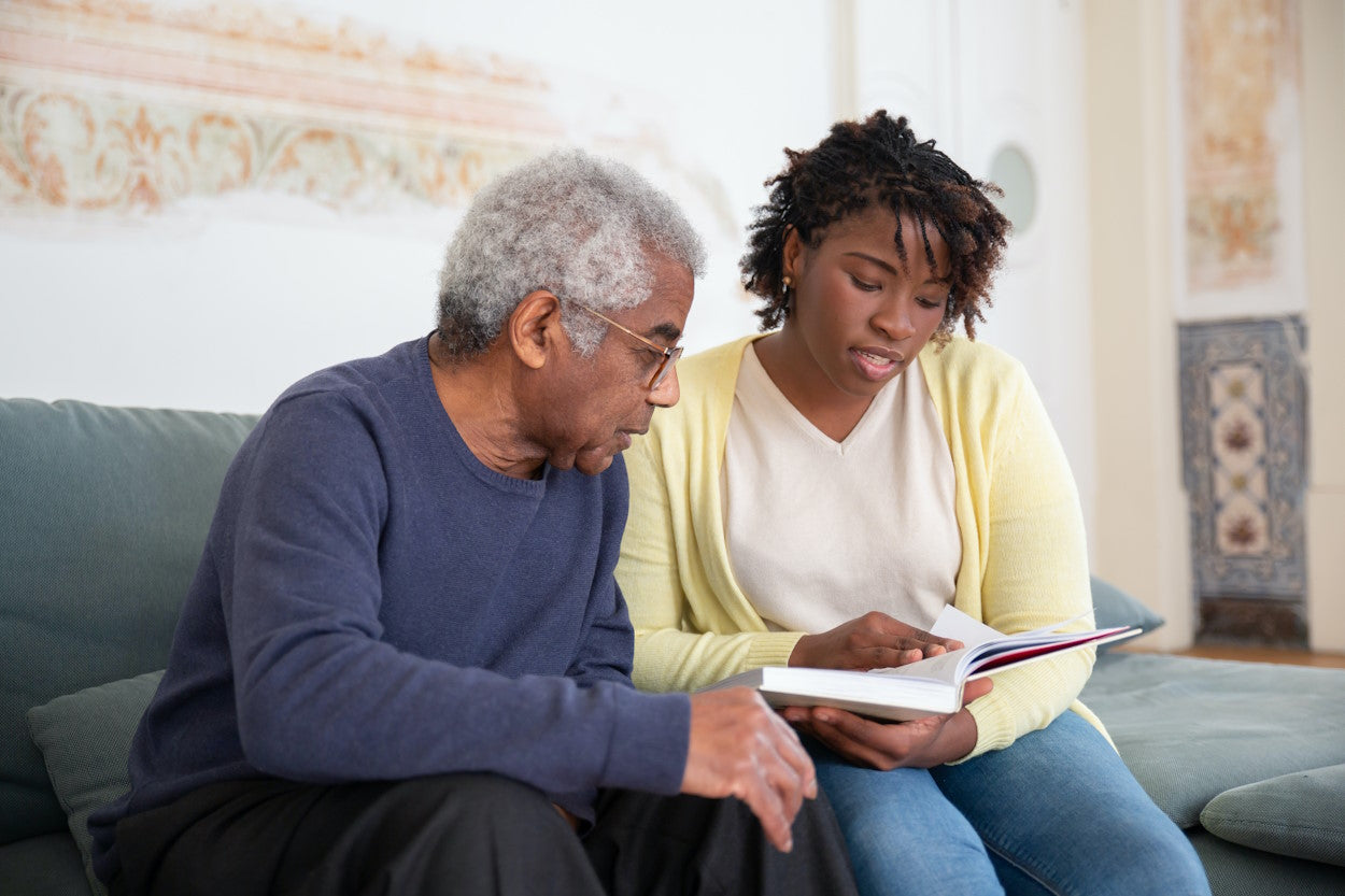 Older man and daughter on couch reading a book