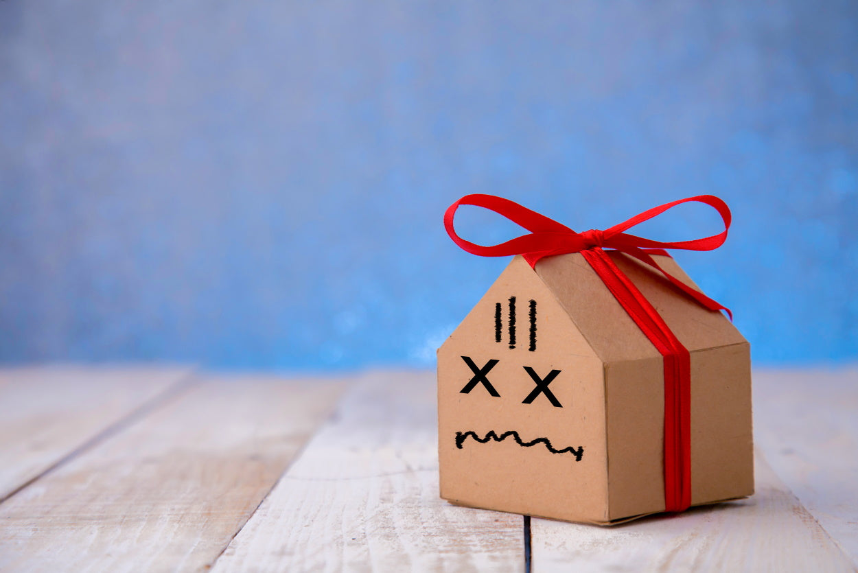 Cardboard box in the shape of a sick house with a frowny face drawn on the front