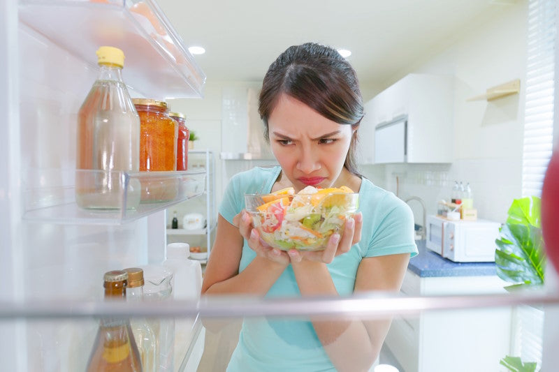 Skeptical woman sniffing old food in the fridge