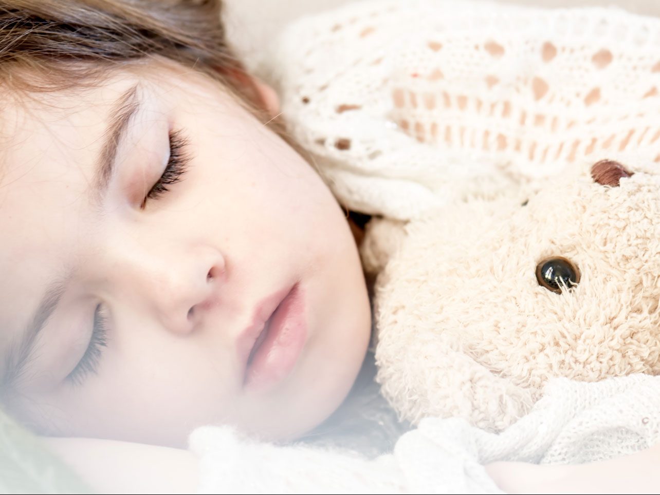 Child sleeping with a stuffed animal in bedroom