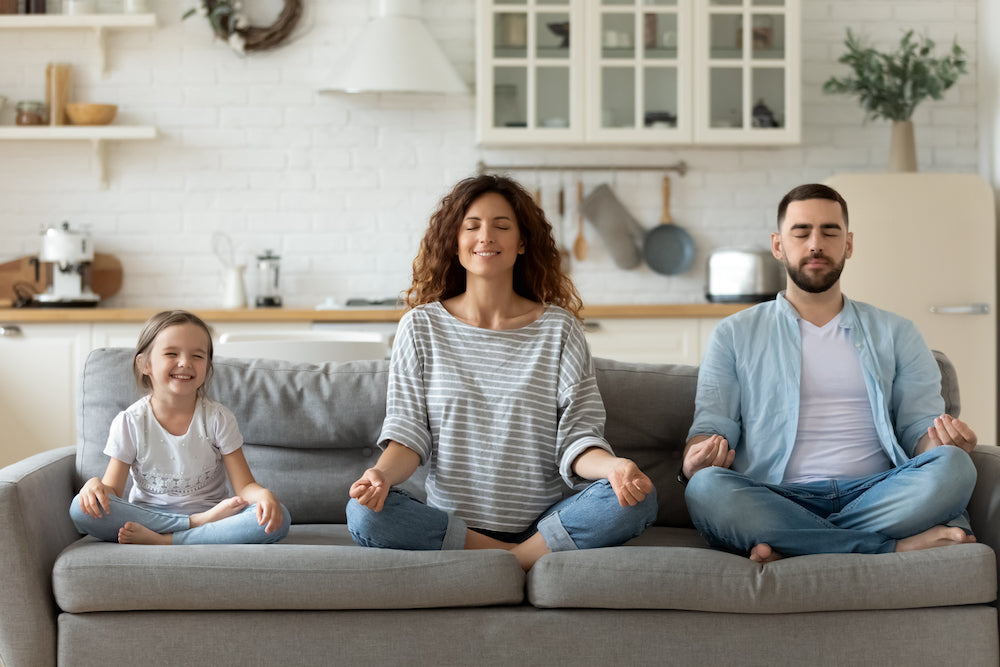 Man, woman, and child sitting cross-legged on the couch with eyes closed and meditating