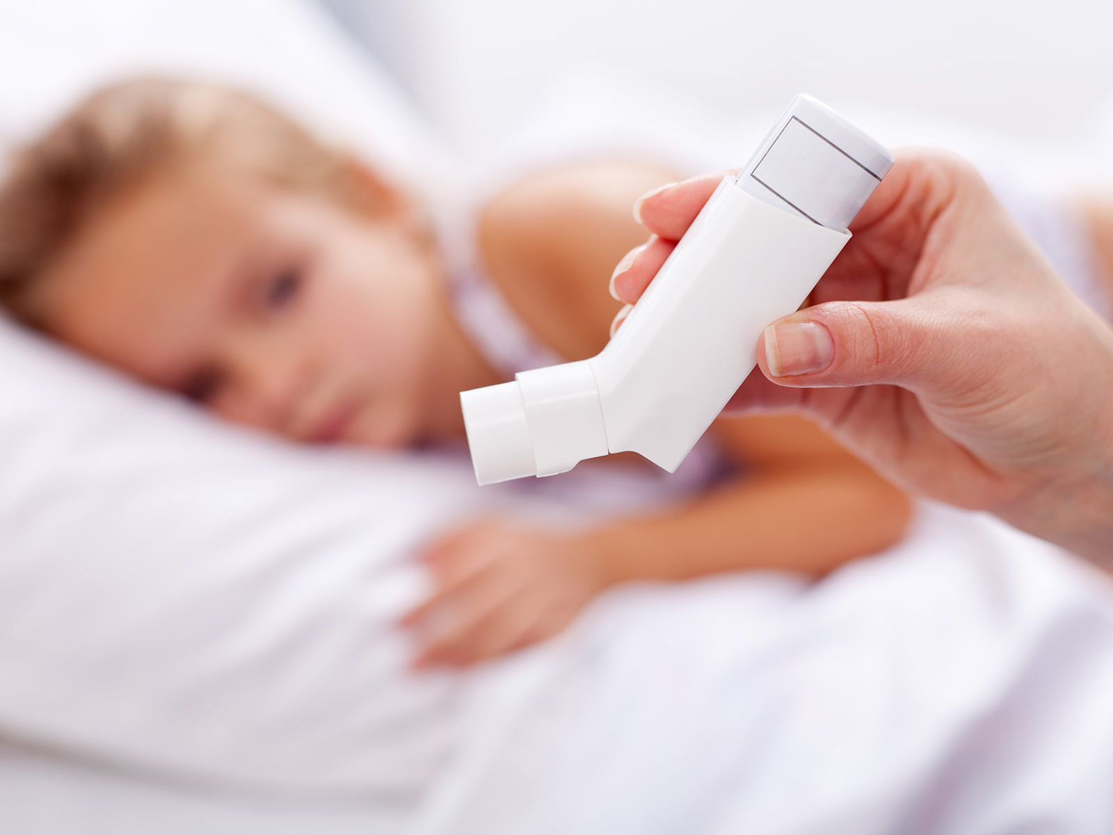 A parent hold an asthma inhaler over a child in bed